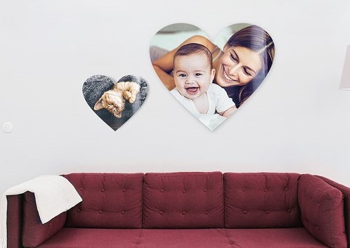 Heartshaped photo wallart hung up over a red sofa, one showing a mum with ther baby, the other one showing a cat