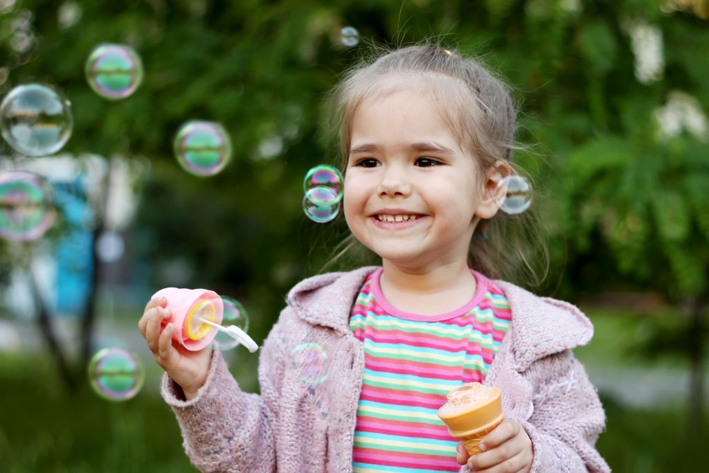 Portrait photo of a small girl, smiling while making soap bubble