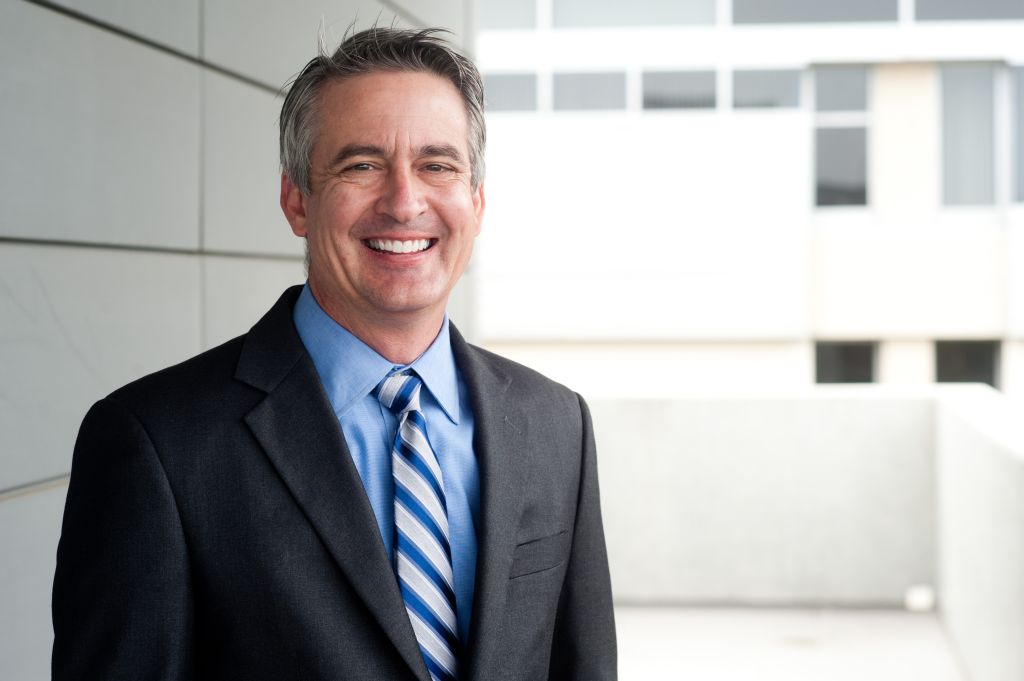Professional headshot photography of a businessman in front of an office building, smiling in the camera