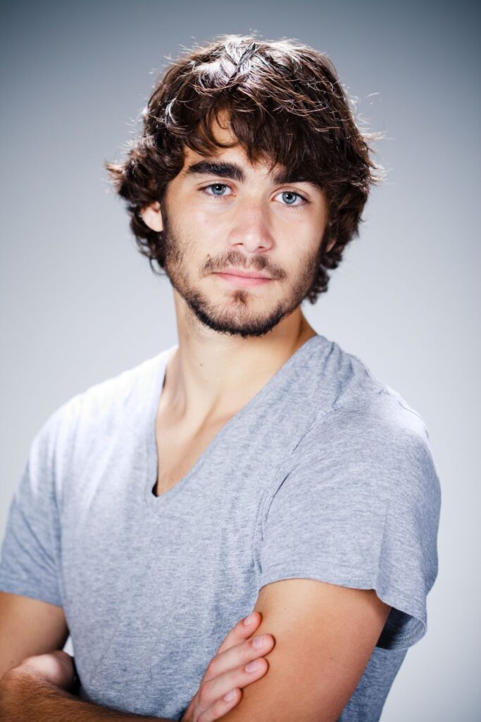 Authentic upper body portrait of a young man with brown hair, crossing his arms