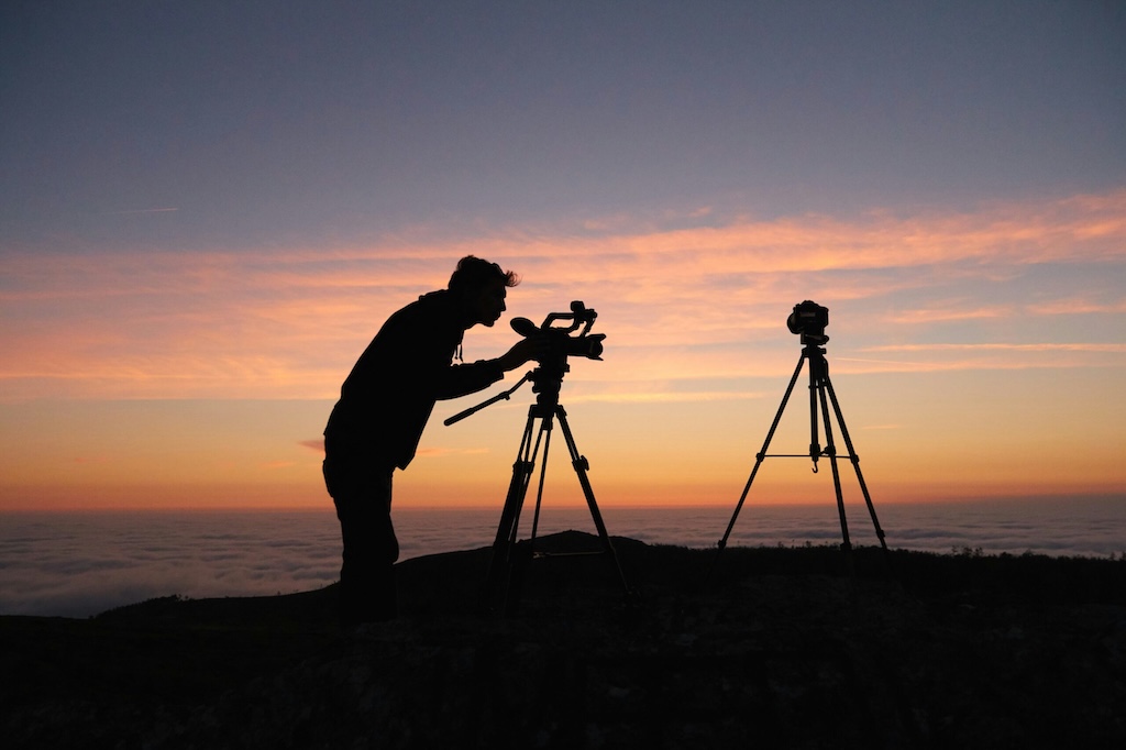 Man doing mountain photography in the mounatins during sunrise with two tripods in front of colorful sky